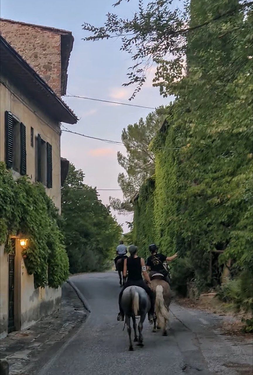 Riders seen from behind along a road between ivy-covered buildings
