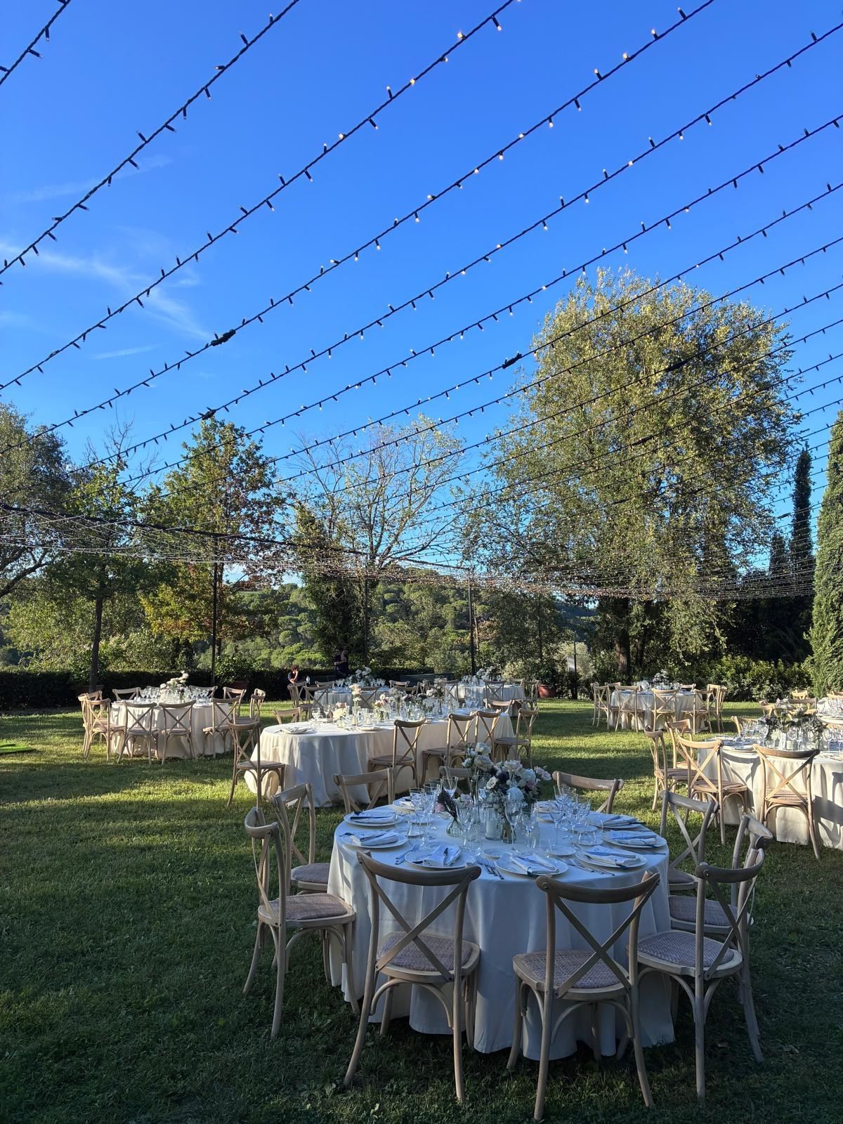 Tavoli rotondi apparecchiati sul prato del giardino sotto file di luci
