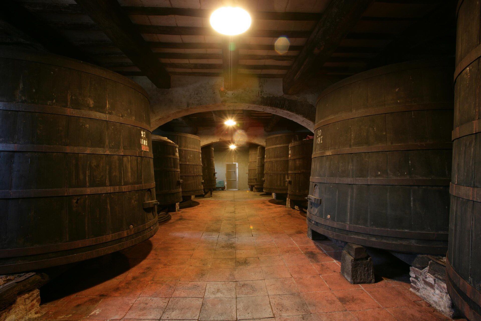 Grandi tini di legno ai lati di una tinaia toscana con il pavimento in cotto